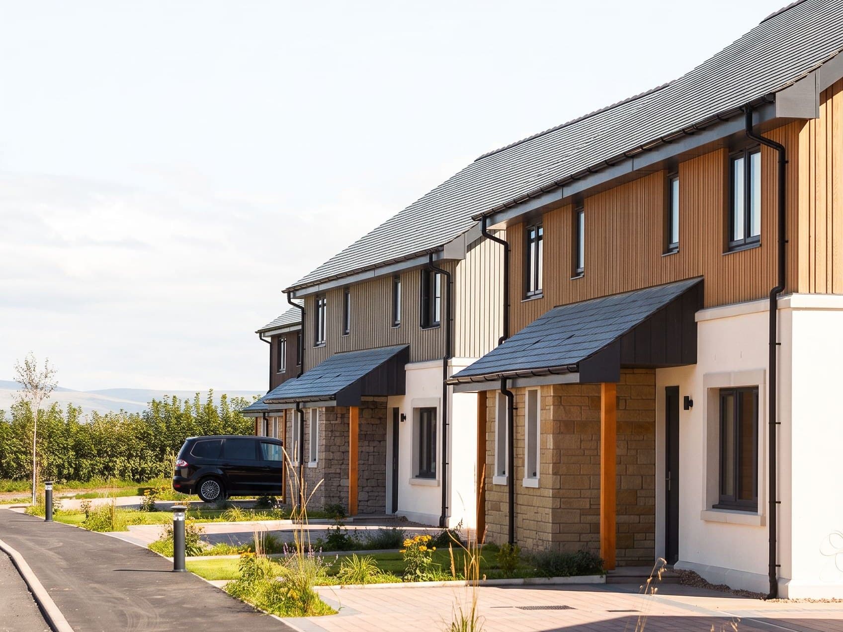 A terrace of completed Hackthorpe homes along a new street — stone porches, timber cladding and slate roofs, with the Pennines on the horizon