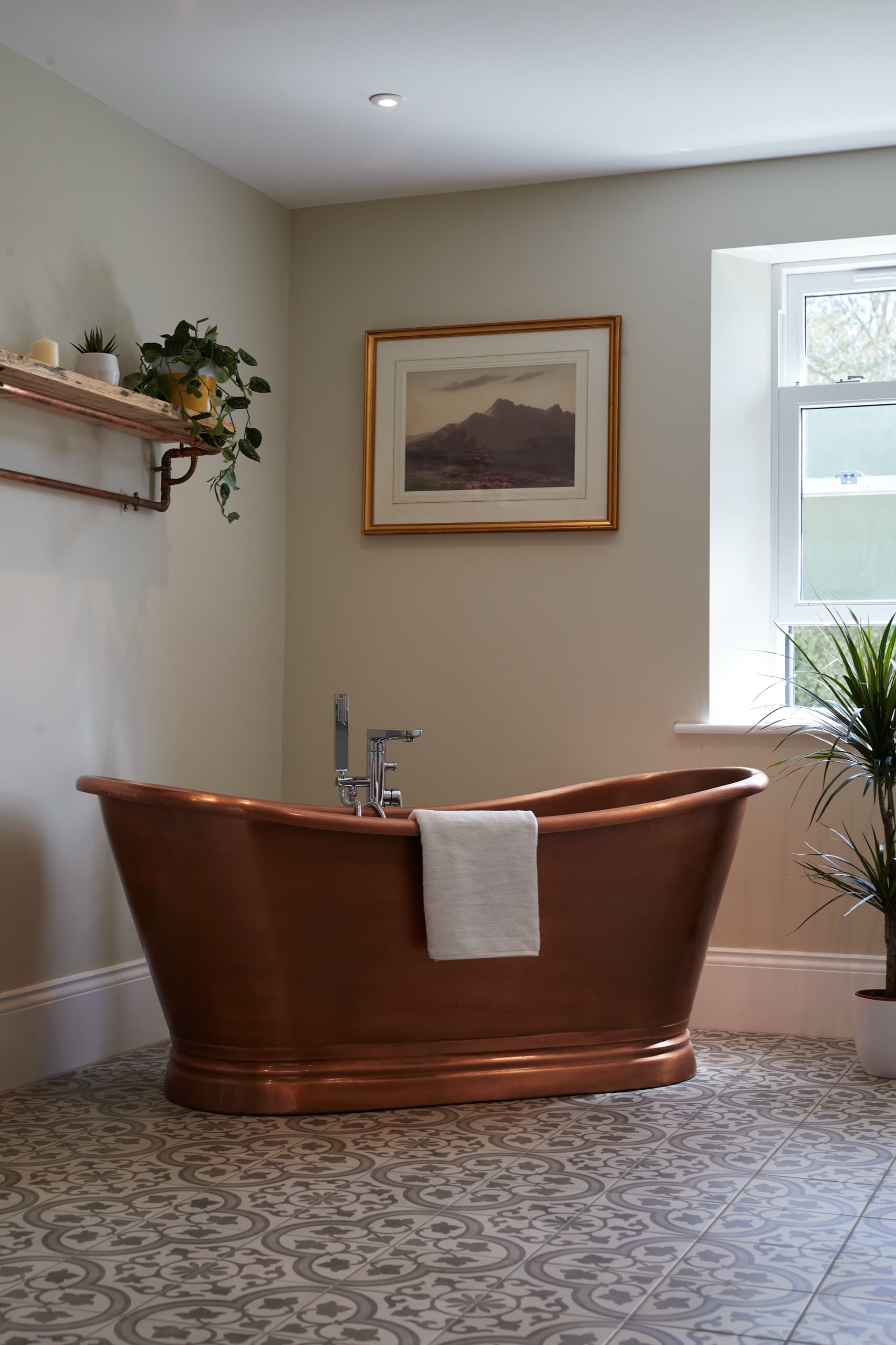 A freestanding copper bath beneath framed Lakeland artwork