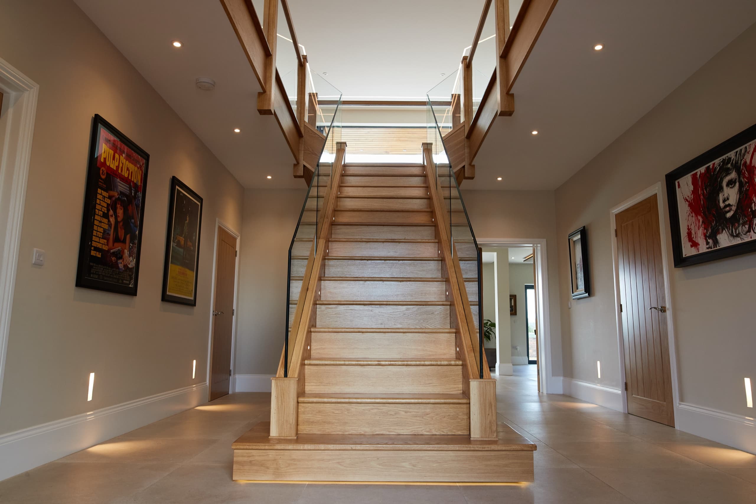 An oak-and-glass staircase rising through a top-lit hall