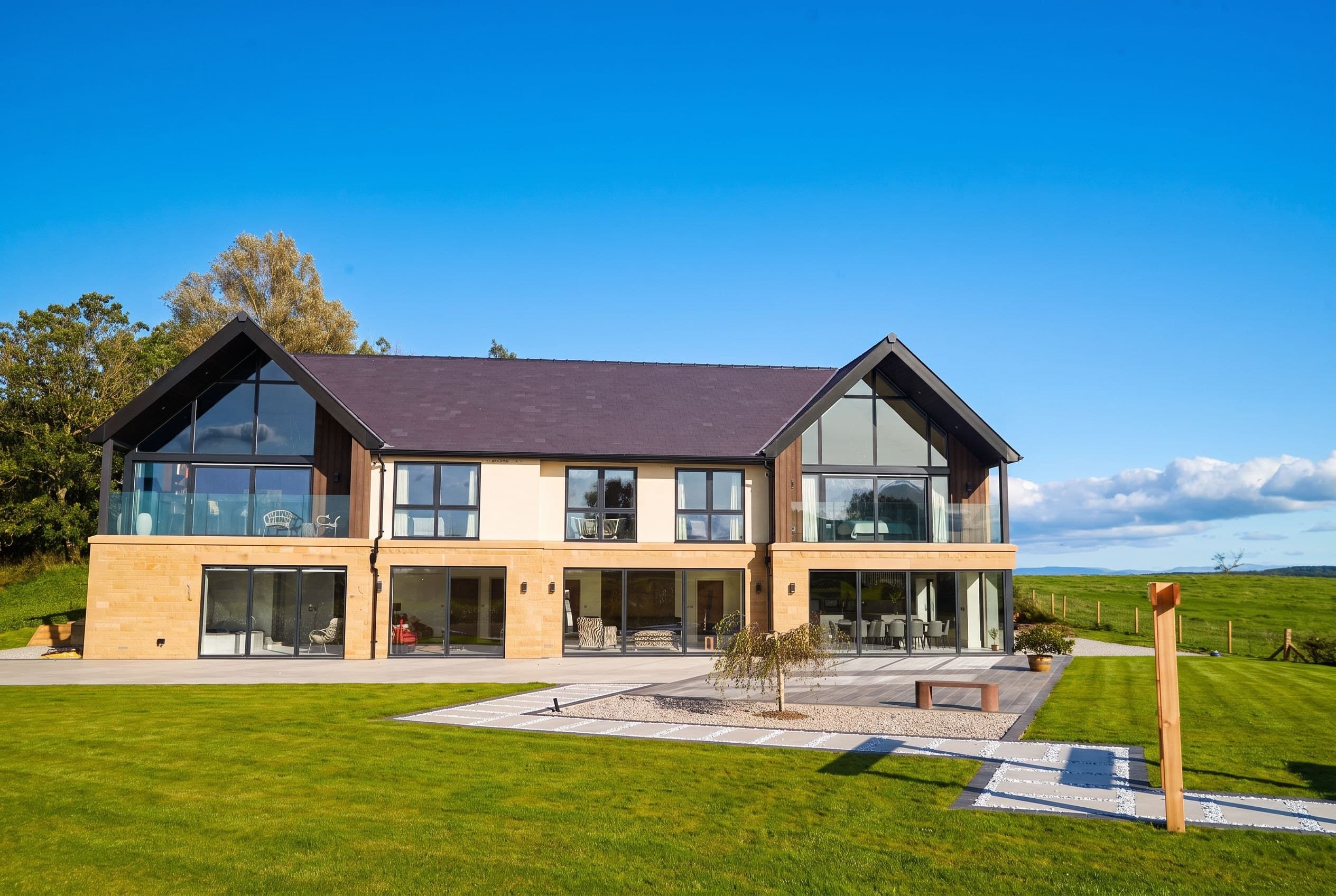 An individually designed contemporary Stoneswood home — twin glazed gables and sandstone detailing above a landscaped terrace